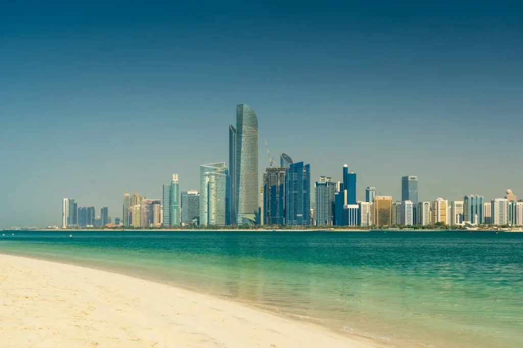 Abu Dhabi felhőkarcolói a tenger túloldalán, homokos parttal