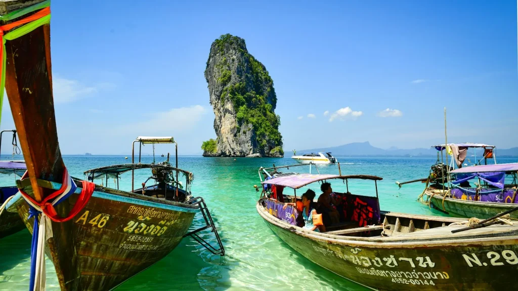 Longtail hajók a türkiz vízben egy mészkősziget előtt, Thaiföld