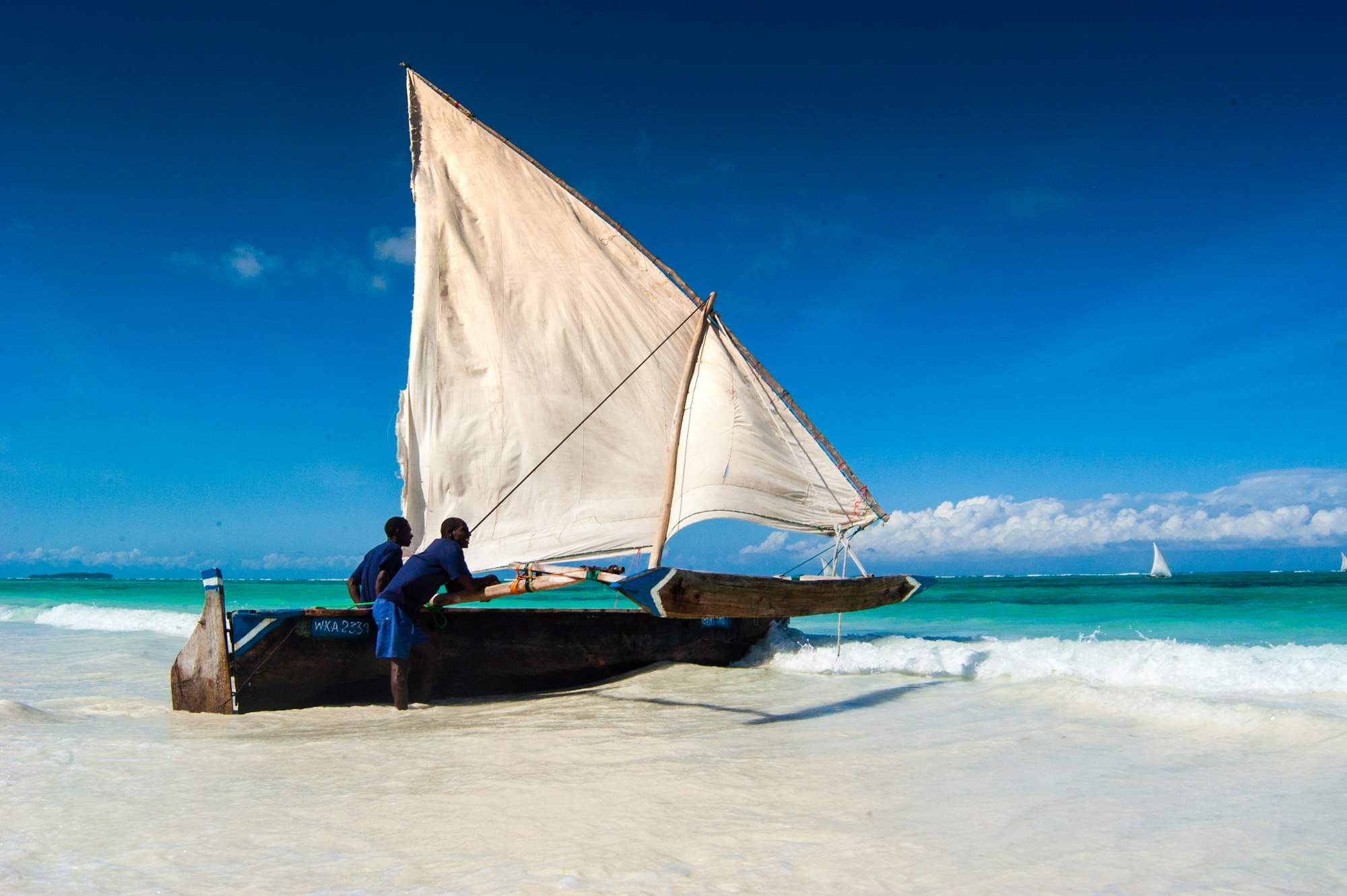 Halászok vitorlás dhow-hajót tolnak a vízre a zanzibári Matemwe strandján